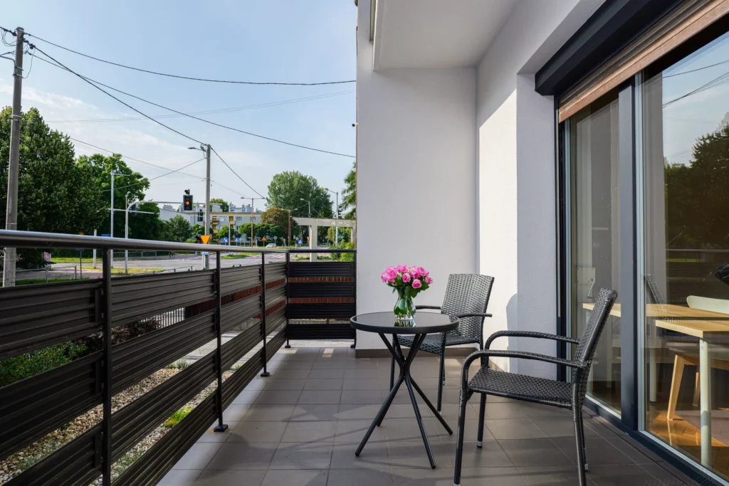 Balkon ze stolikiem i wiklinowymi fotelami, widok na skrzyżowanie i zieleń, słoneczny dzień