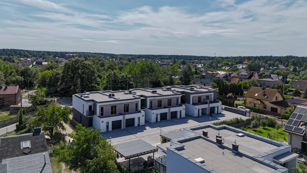 Osiedle domów szeregowych z lotu ptaka na tle zabudowy i lasu, ukośny kadr lotniczy latem