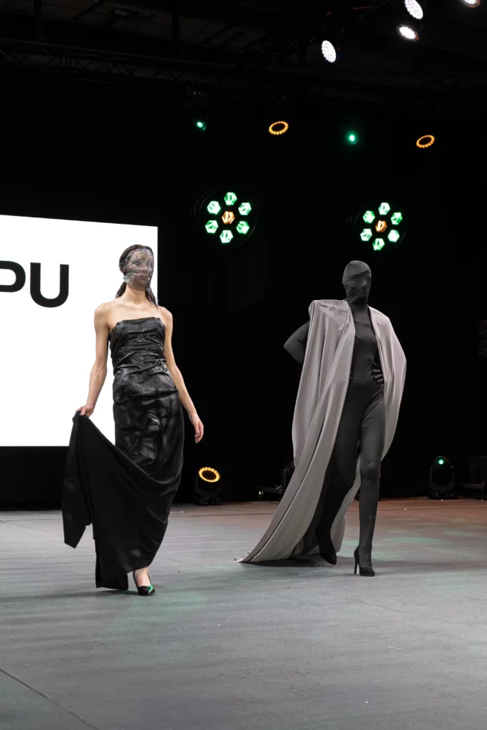Model w kapeluszu kowbojskim i krótkiej kurtce oraz modelka w minimalistycznym staniku, gotycki streetwear na wybiegu