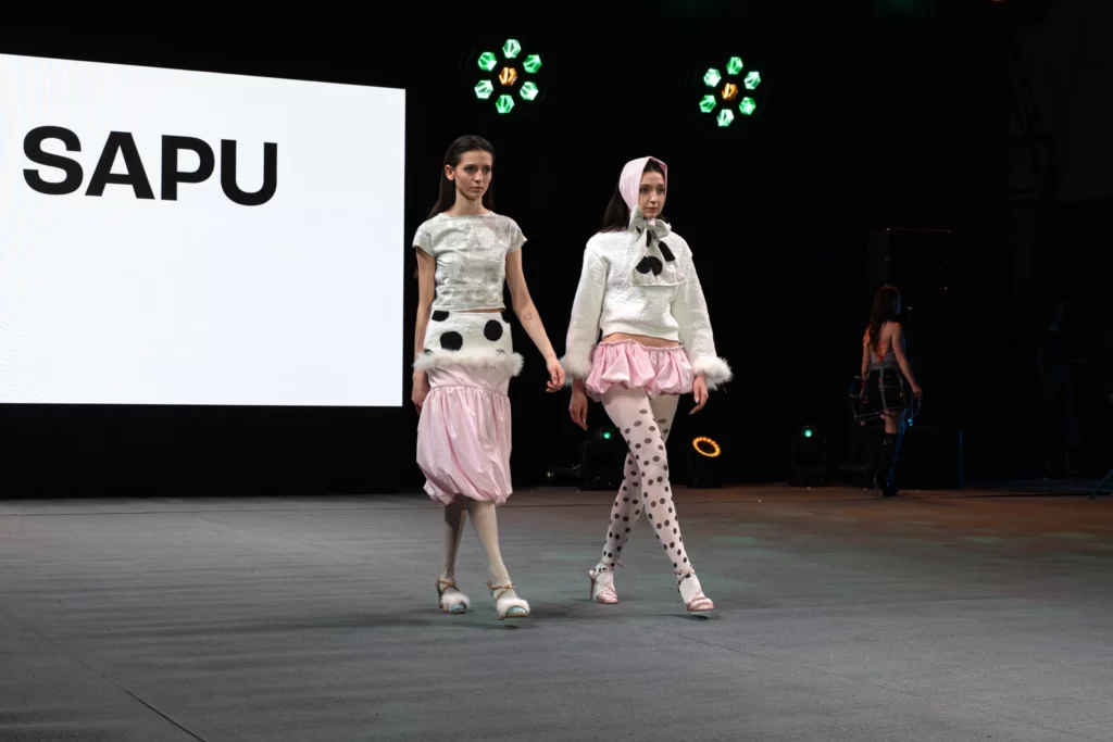 Dwie modelki w białych górach i różowych bufiastych spódnicach z futrzaną lamówką, lalkowa stylizacja, zielone reflektory