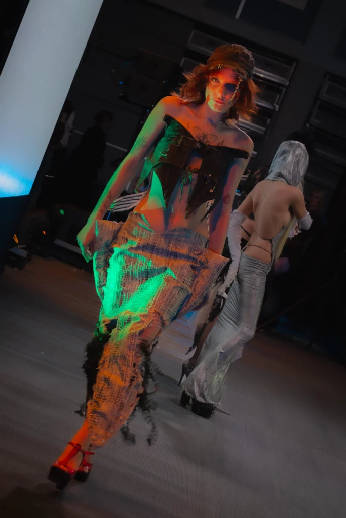 Model z teatralną maską w dłoni i pikowanej satynowej narzutce, druciany naszyjnik, niebieskie sceniczne światło