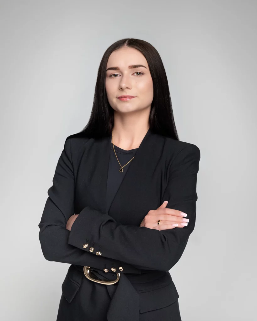 Portret biznesowy kobiety w czarnym żakiecie ze skrzyżowanymi rękami i złotym naszyjnikiem